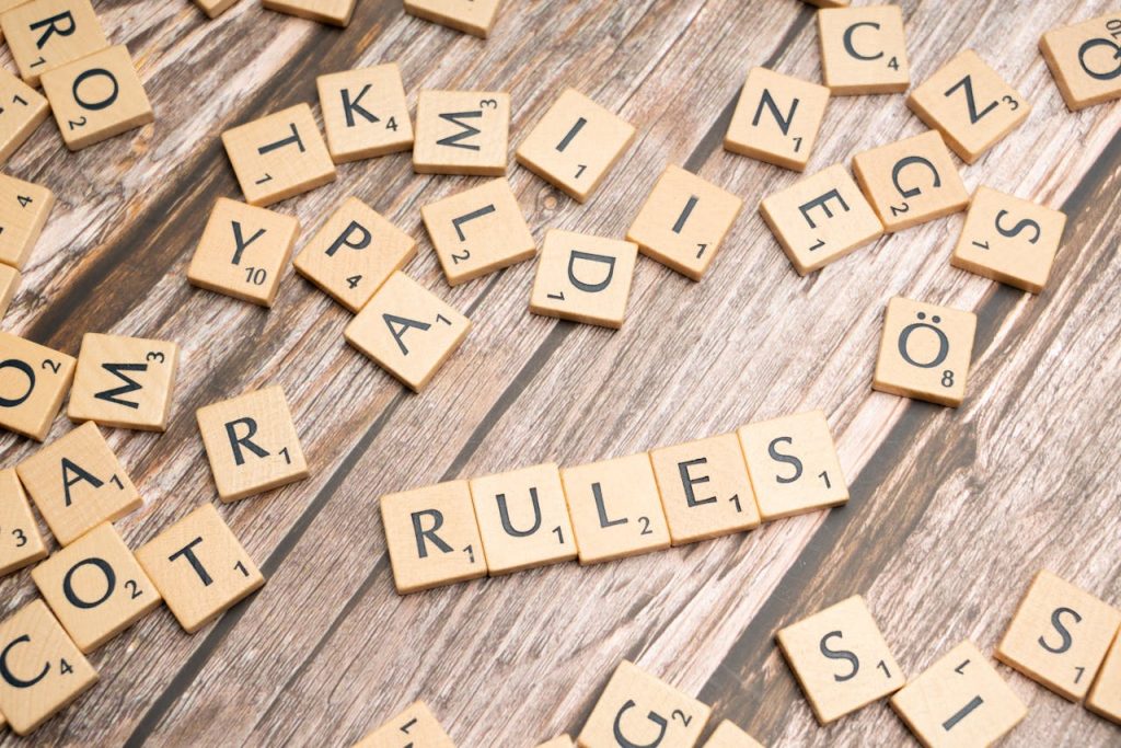 Wooden letter tiles arranged to spell 'Rules' on a textured wooden background.